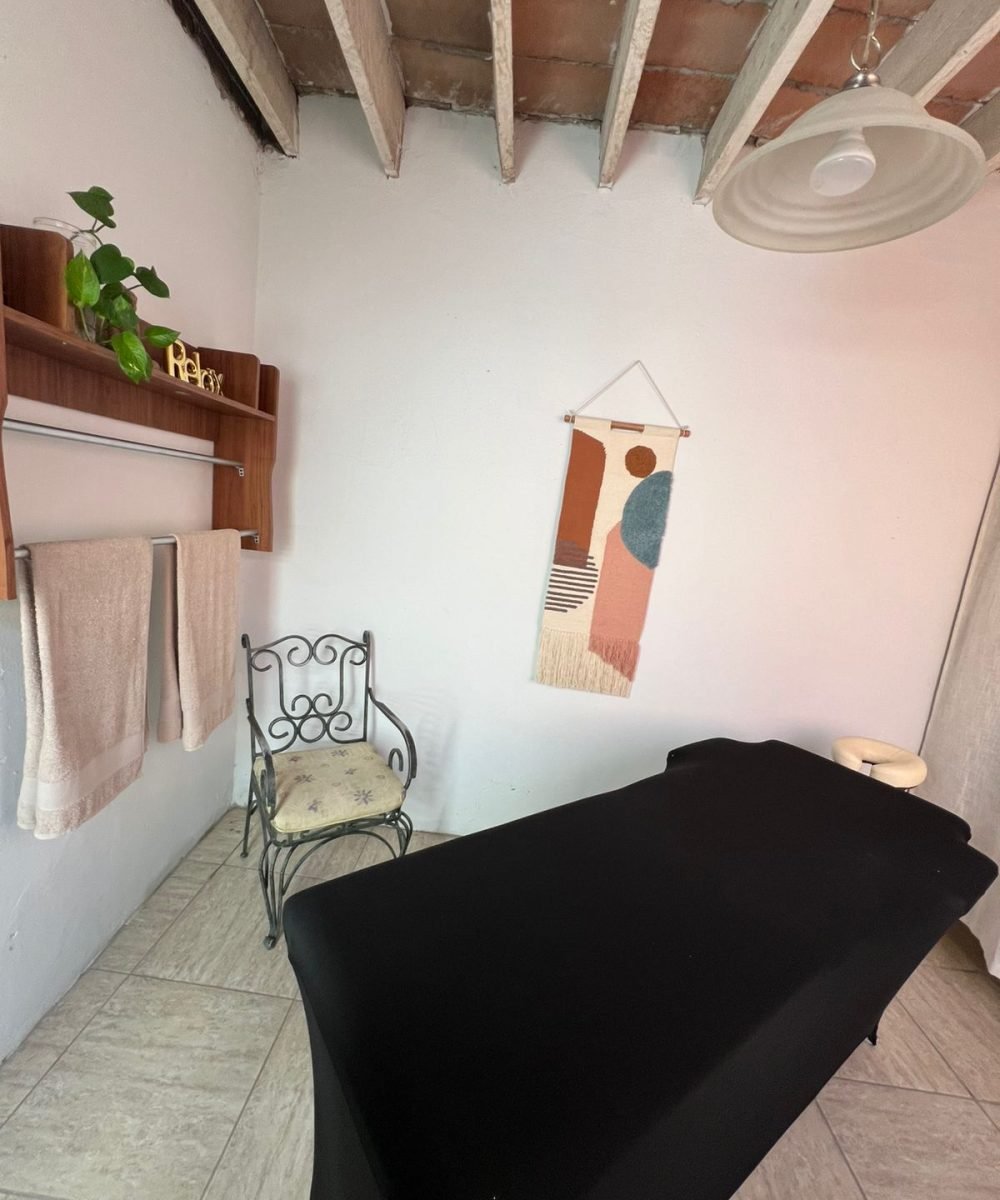 cama de masajes con silla verde al lado y colgador, es una vista panoramica del cuarto de masajes